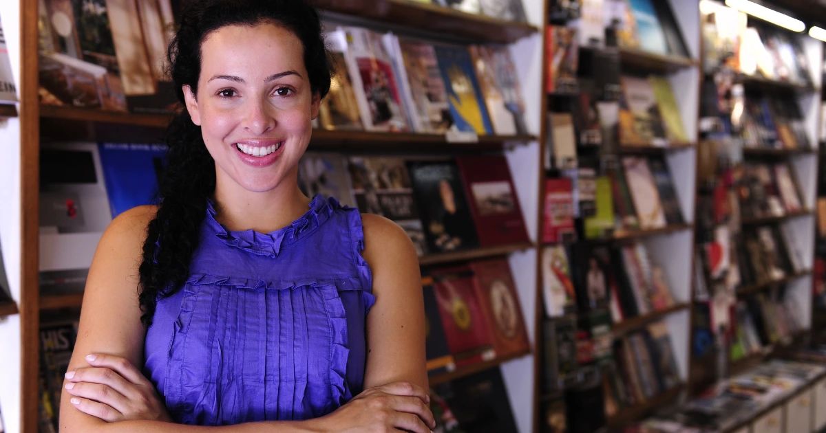 Smiling woman with arms crossed standing in front of packed bookshelves in an independent bookshop