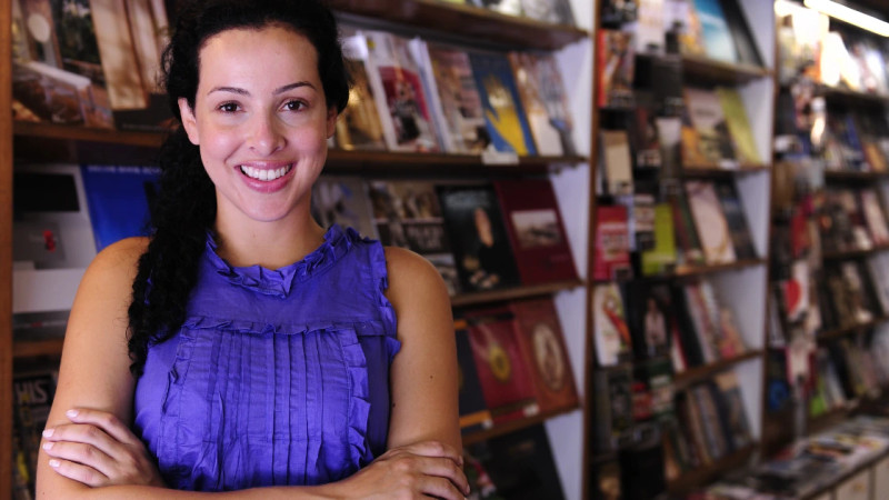 Smiling woman with arms crossed standing in front of packed bookshelves in an independent bookshop