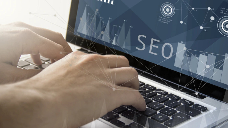 Hands typing on a laptop with an SEO analytics dashboard overlay showing bar charts and data visualisations