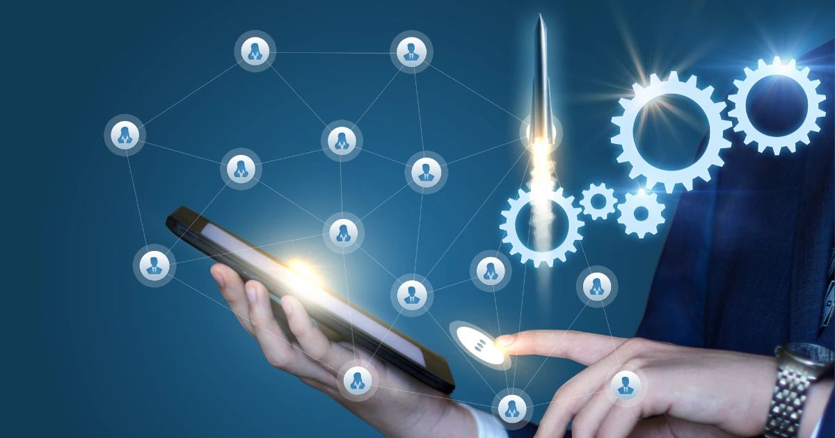 Suited person holding smartphone with glowing digital network icons, rocket and gear graphics overlaid on blue background