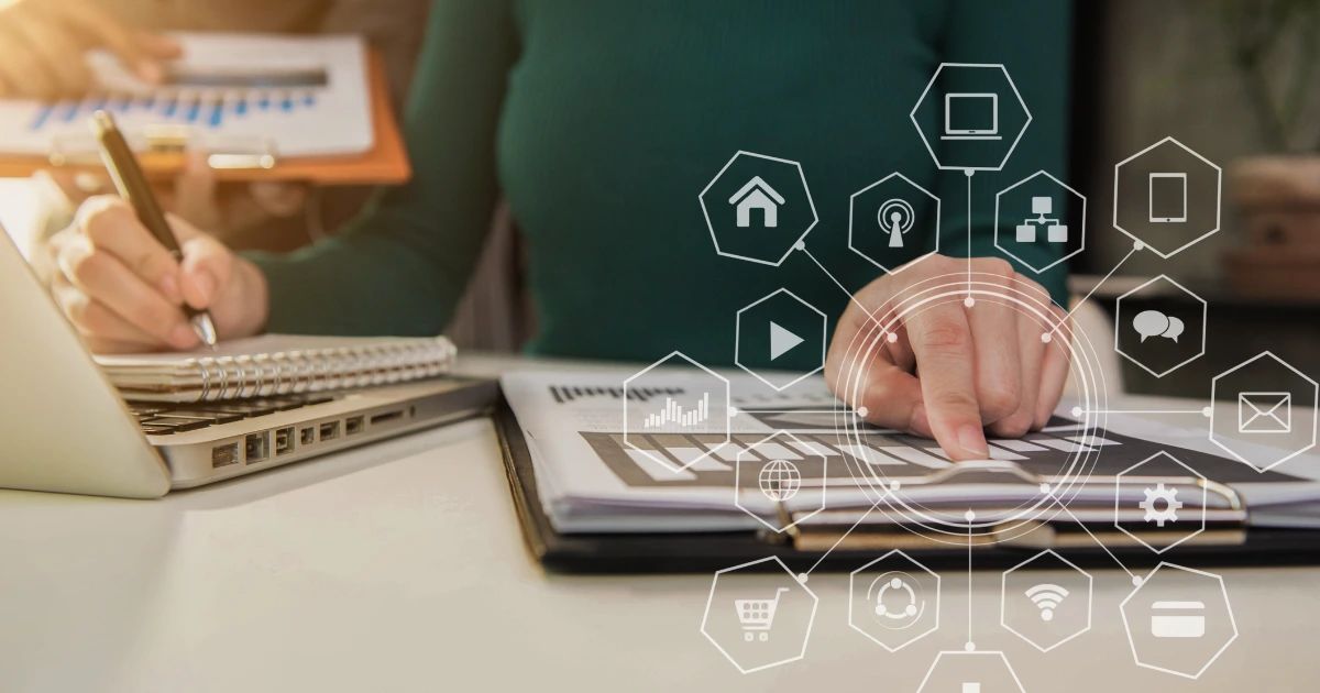 Person pointing at document on desk beside laptop, with digital connectivity icons overlaid in foreground
