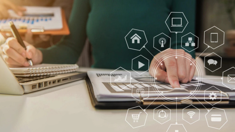 Person pointing at document on desk beside laptop, with digital connectivity icons overlaid in foreground