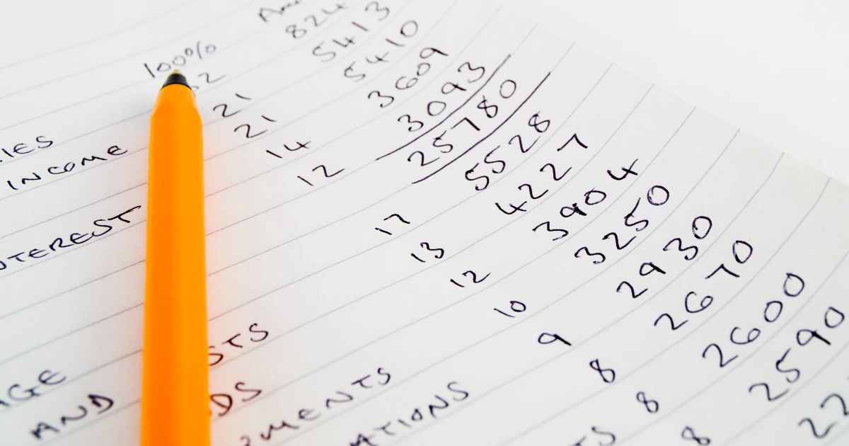Close-up of handwritten financial figures on lined paper with an orange pen, showing income and interest columns
