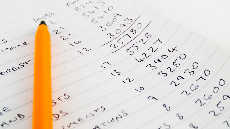 Close-up of handwritten financial figures on lined paper with an orange pen, showing income and interest columns