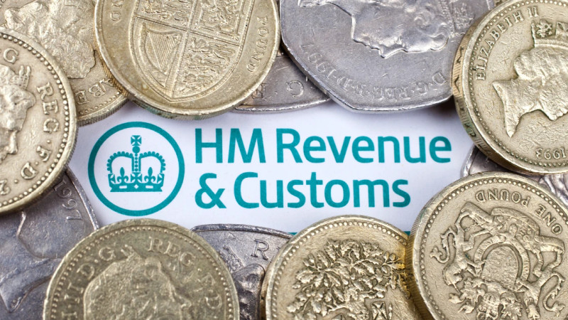 UK pound coins scattered over a printed HM Revenue & Customs document showing the HMRC logo