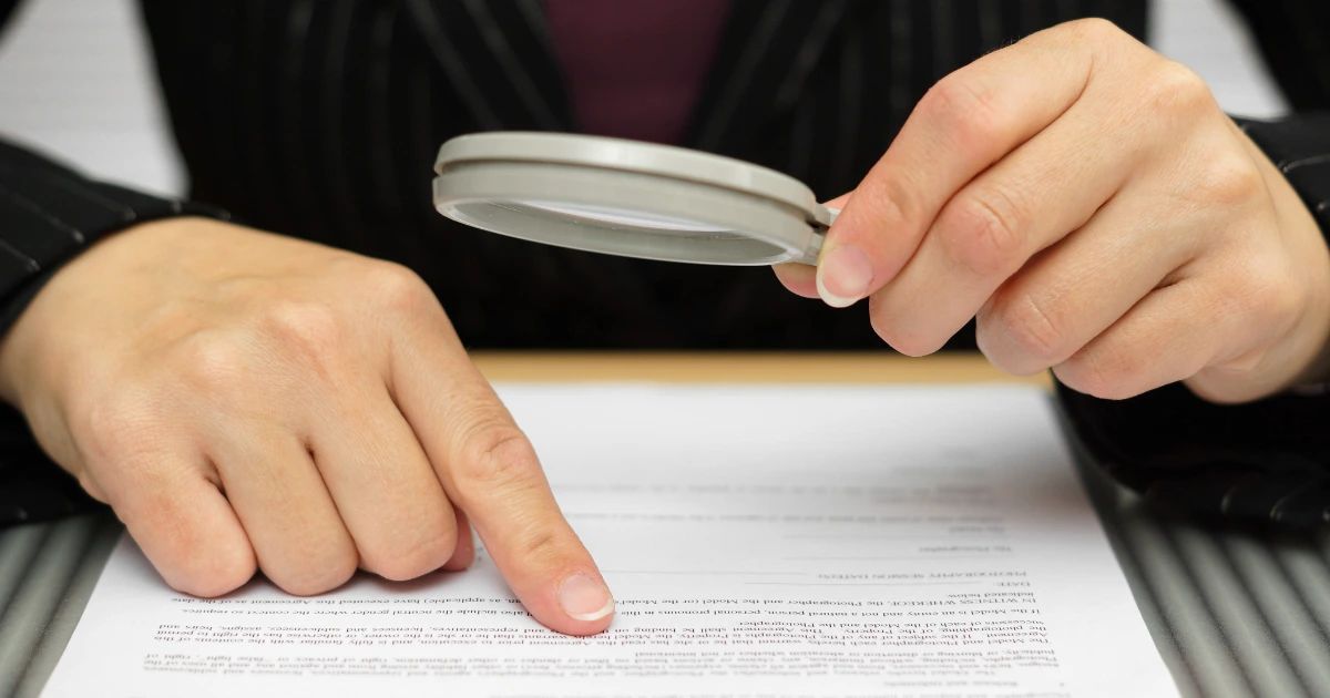 Hands holding a magnifying glass over a printed legal document, with one finger pointing at the text