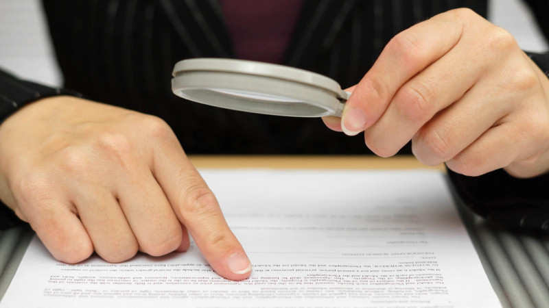 Hands holding a magnifying glass over a printed legal document, with one finger pointing at the text