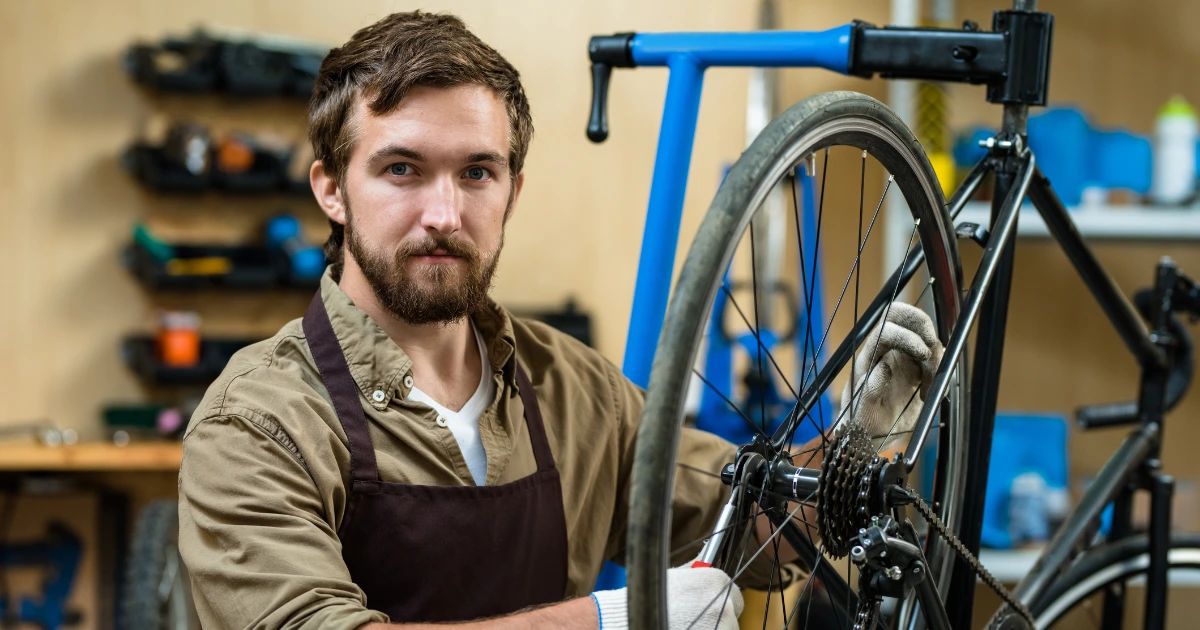 Bearded man in apron and work gloves servicing a road bicycle wheel in a workshop