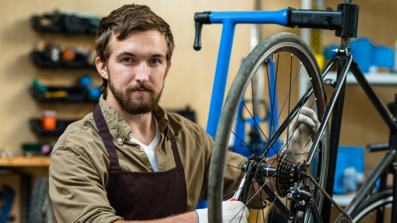 Bearded man in apron and work gloves servicing a road bicycle wheel in a workshop