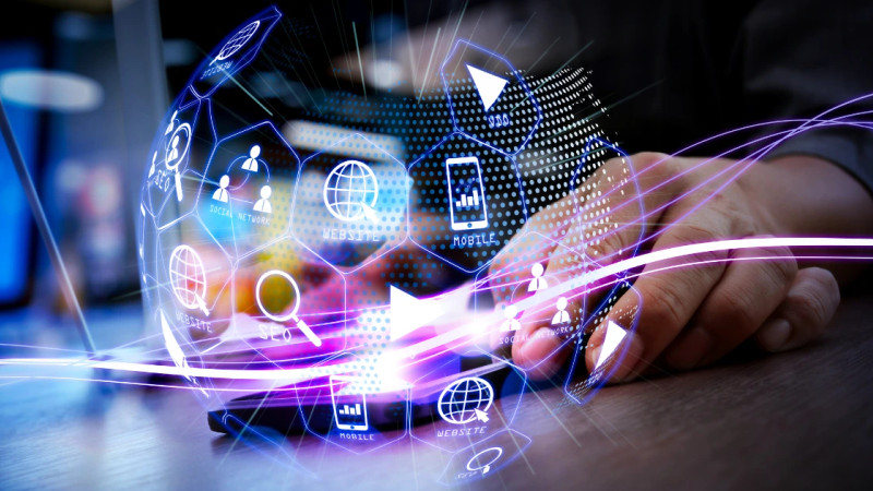 Hands on a desk with a glowing holographic sphere of digital marketing icons including SEO, website, mobile and social
