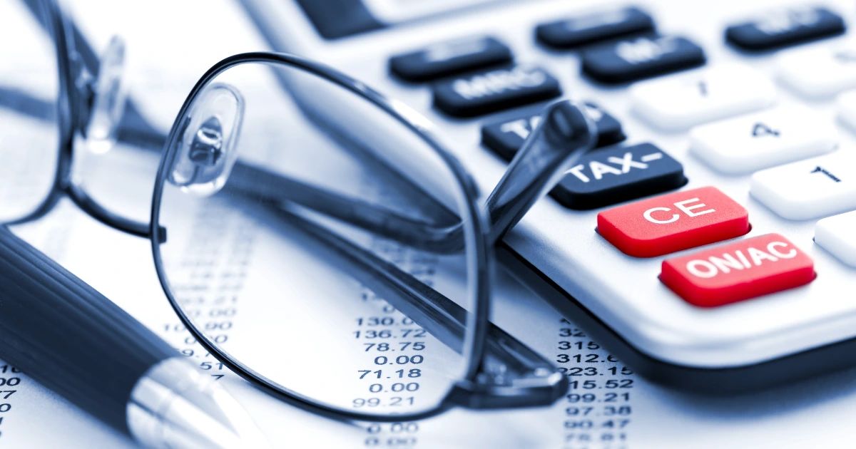 Close-up of a tax calculator with red keys, reading glasses and a pen resting on a printed financial statement