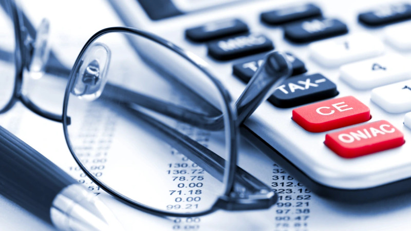Close-up of a tax calculator with red keys, reading glasses and a pen resting on a printed financial statement