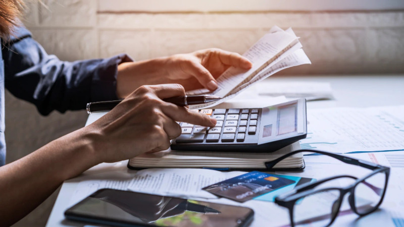 Person holding receipts and using a calculator at a desk with financial papers, credit cards and glasses nearby
